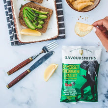 Savoursmiths  - Somerset Cheddar and Shallot Luxury Potato Crisps next to a plate of brown toast and avocado and lemon
