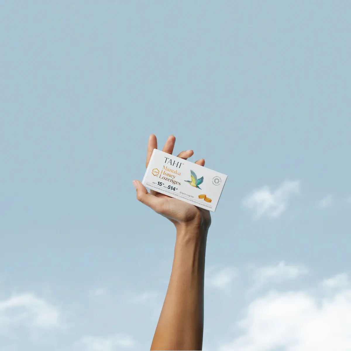 TAHI - Mānuka Lozenges UMF 15+ MGO 514+ Held in a hand against a blue sky