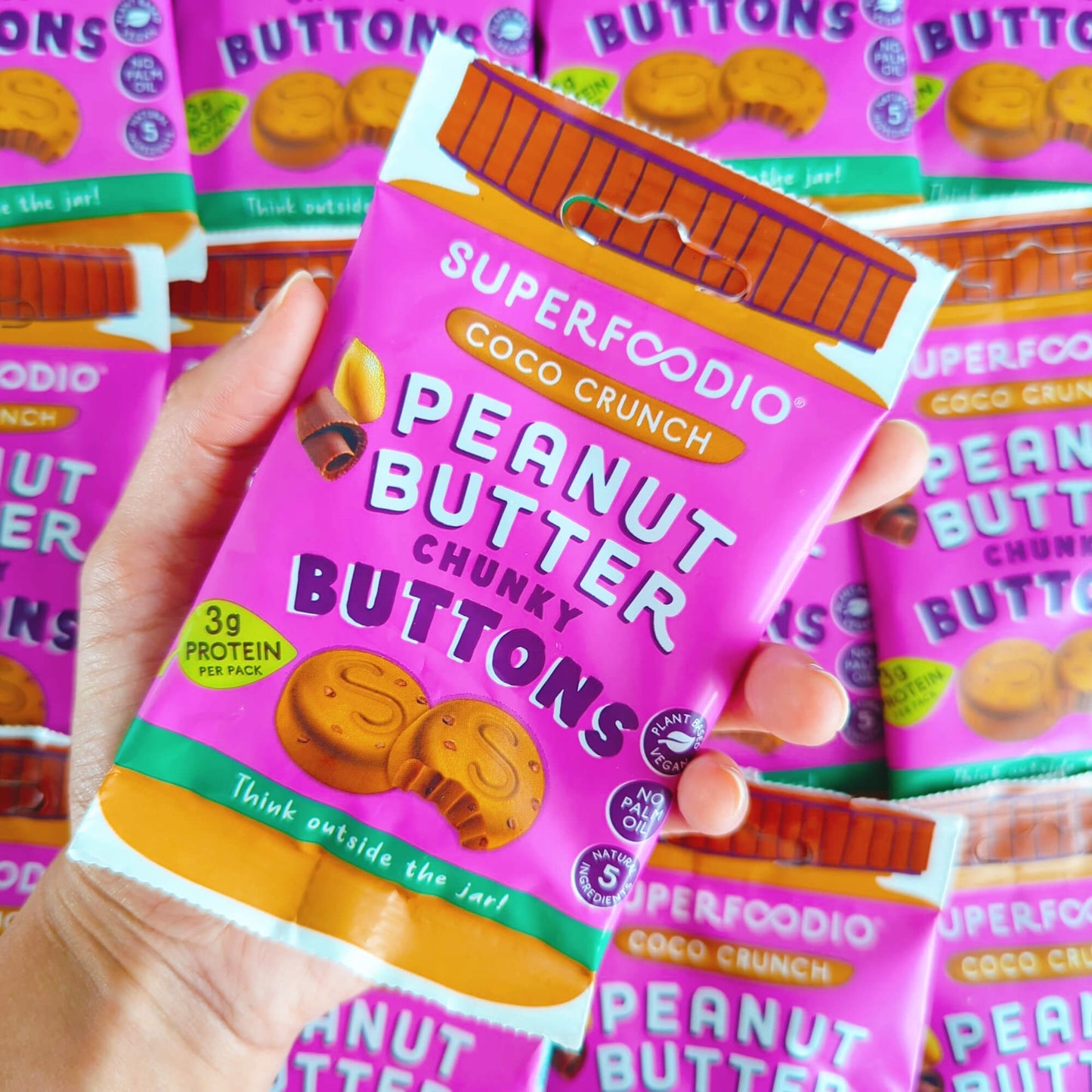 Coco Crunch Peanut Butter Buttons 15 x 20g - Superfoodio. Hand holding a bag of buttons